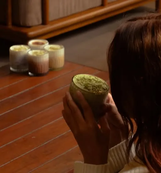 A hand holding an iced matcha cloud on a wooden table