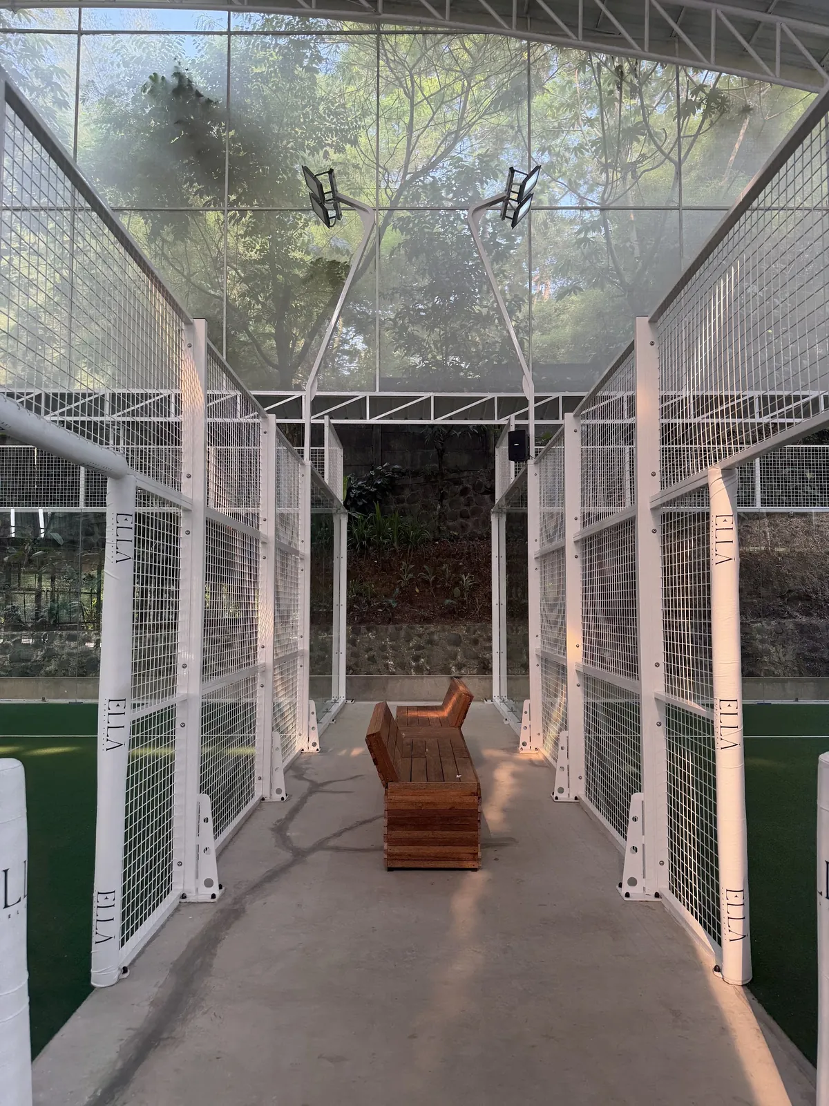 A wooden bench in the walkway between two green courts