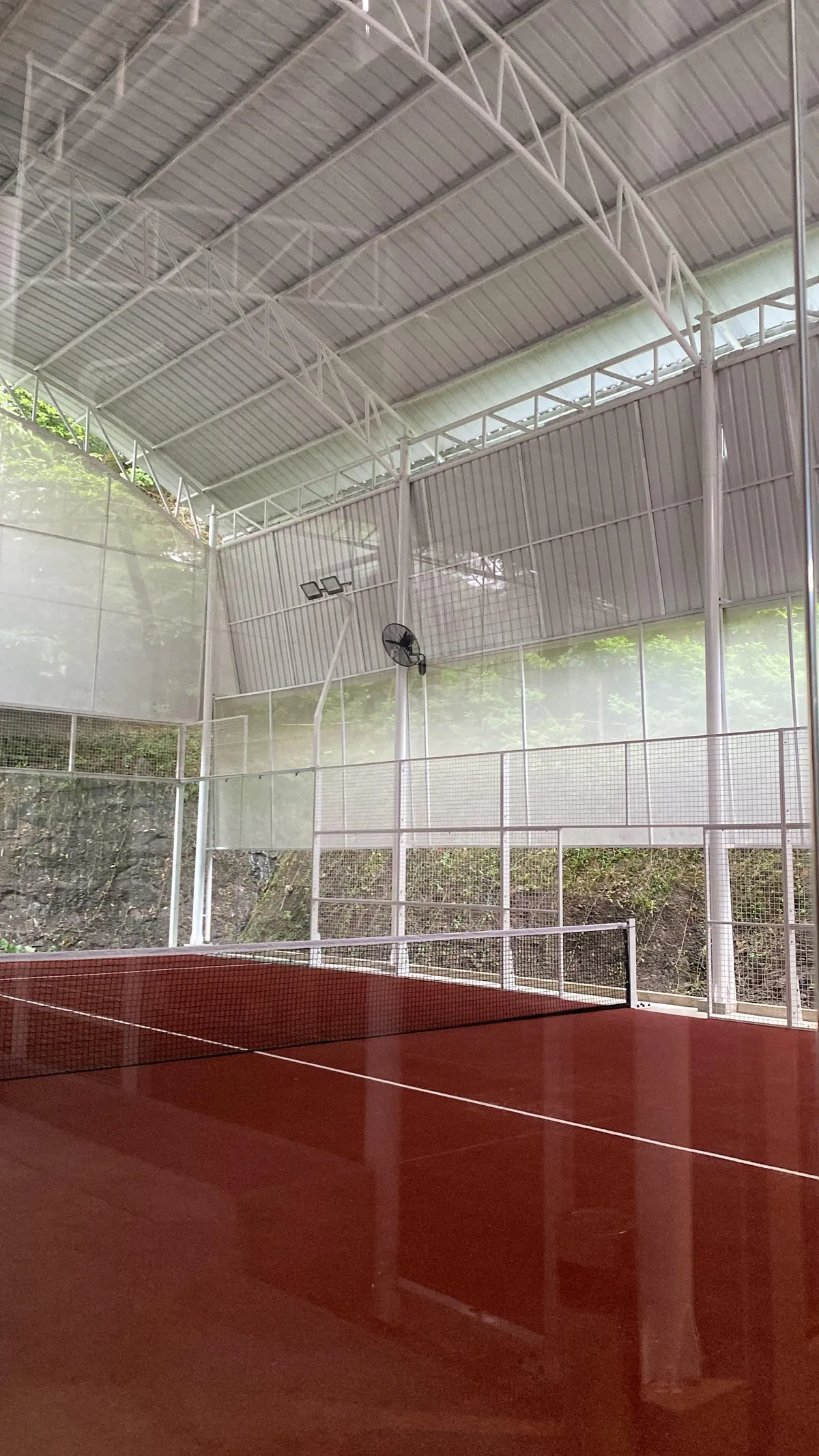 The terracotta court under Ella's white steel roof, with trees beyond the glass